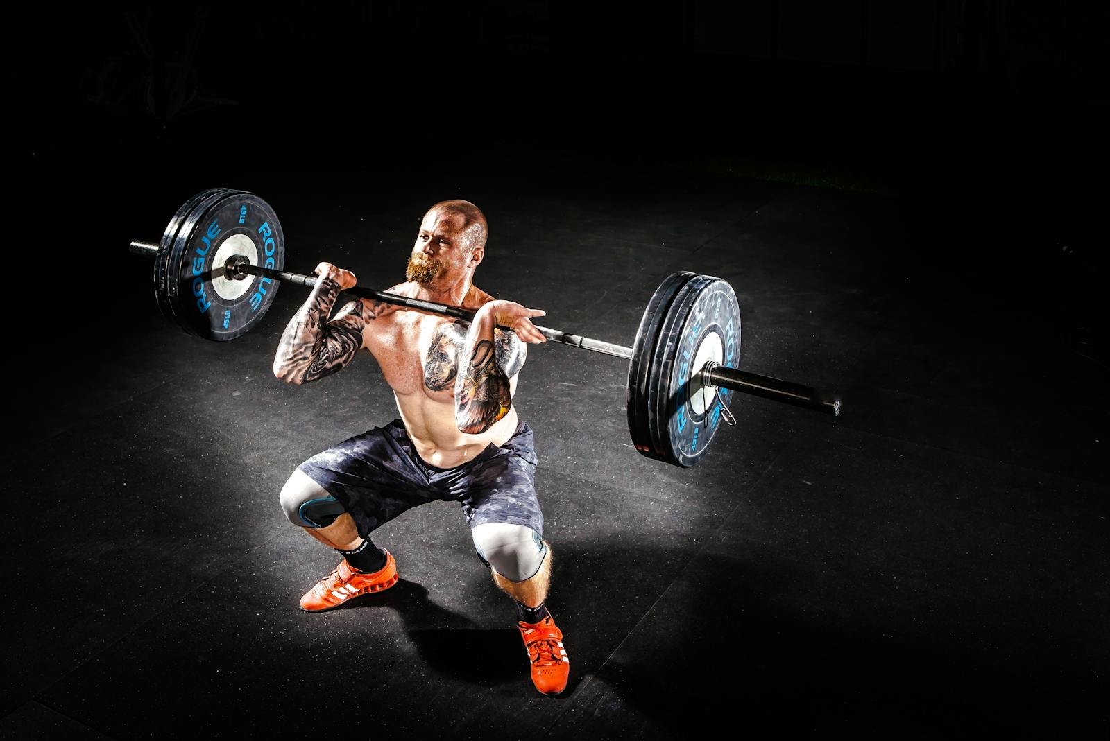 A muscular man performing a power clean exercise in a dimly lit gym.